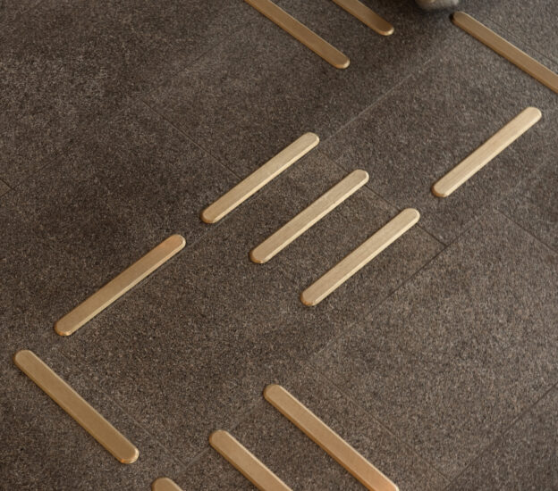 Tactile guidance strips made of brass with a lined surface, installed on dark stone floor