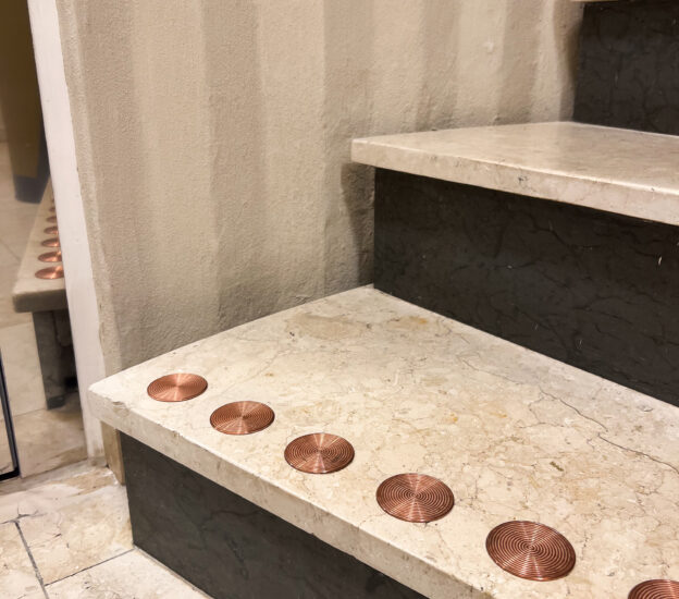 Runda kontrastmarkeringar i koppar på vit stentrapppa i trapphus inomhus